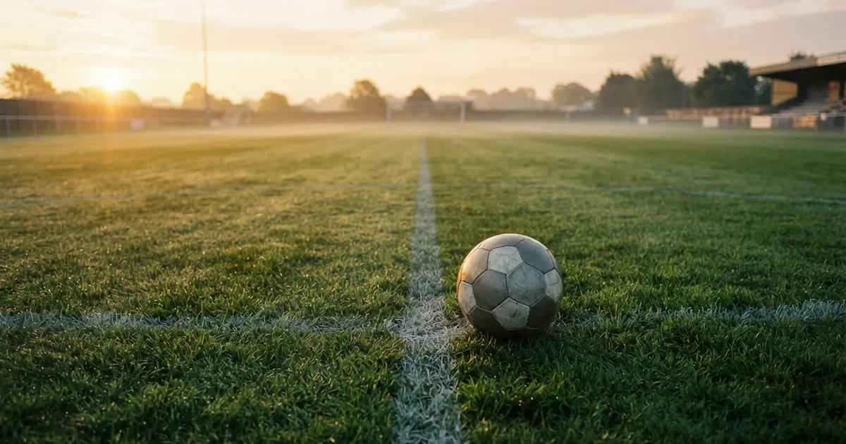 Een voetbal op de middenstip van een grasveld in het ochtendlicht