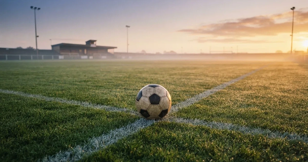 Een voetbal op de middenstip van een grasveld in het ochtendlicht