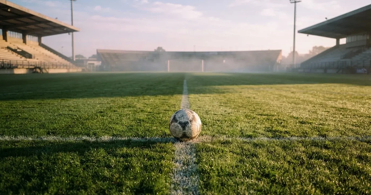 Een voetbal op de middenstip van een grasveld in het ochtendlicht