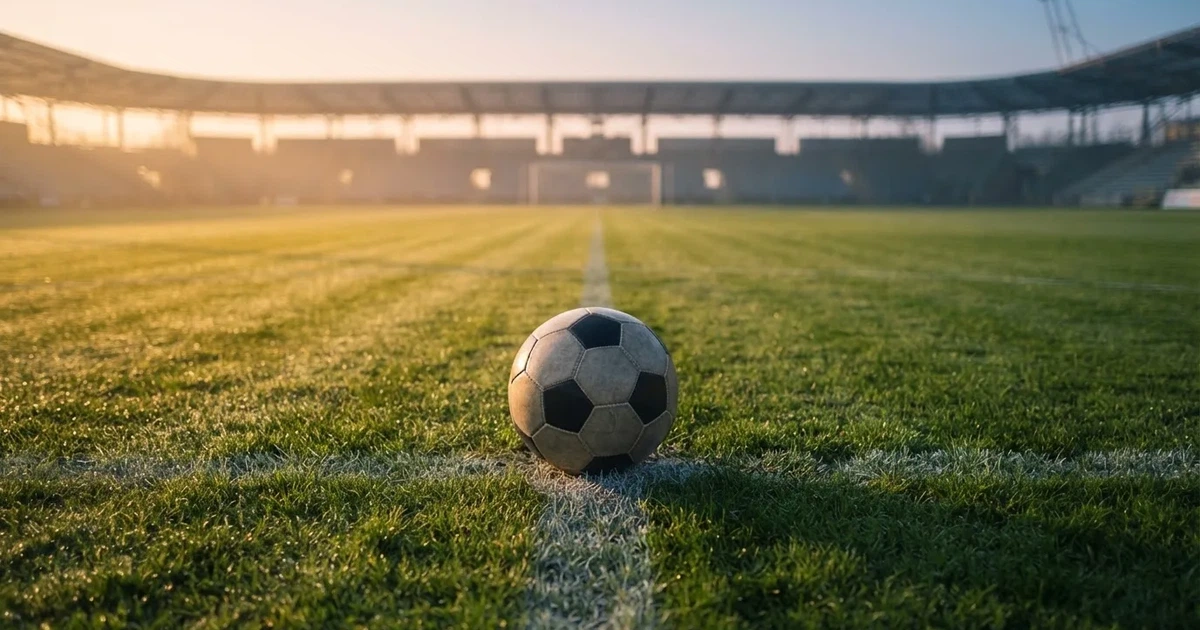 Een voetbal op de middenstip van een grasveld in het ochtendlicht