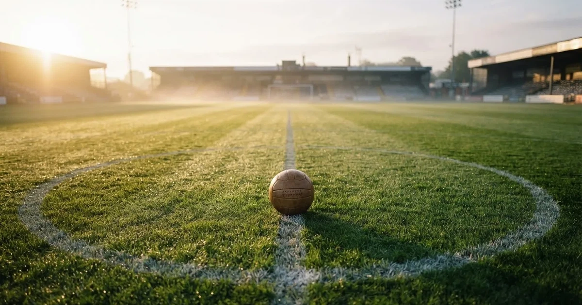 Een voetbal op de middenstip van een grasveld in het ochtendlicht